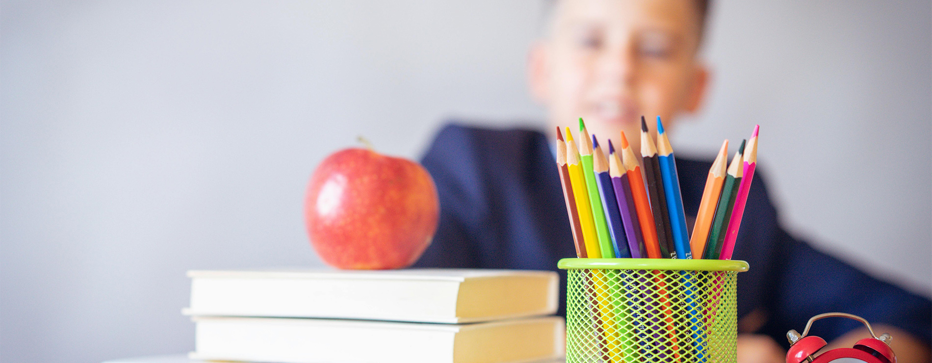 Niño en escuela, lápices de colores, libro y manzana